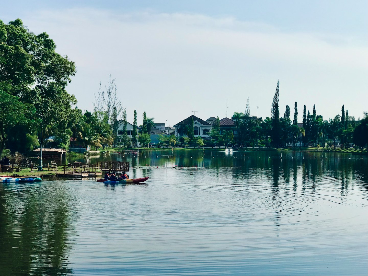 People paddle kayaks on a lake near a residential shoreline.