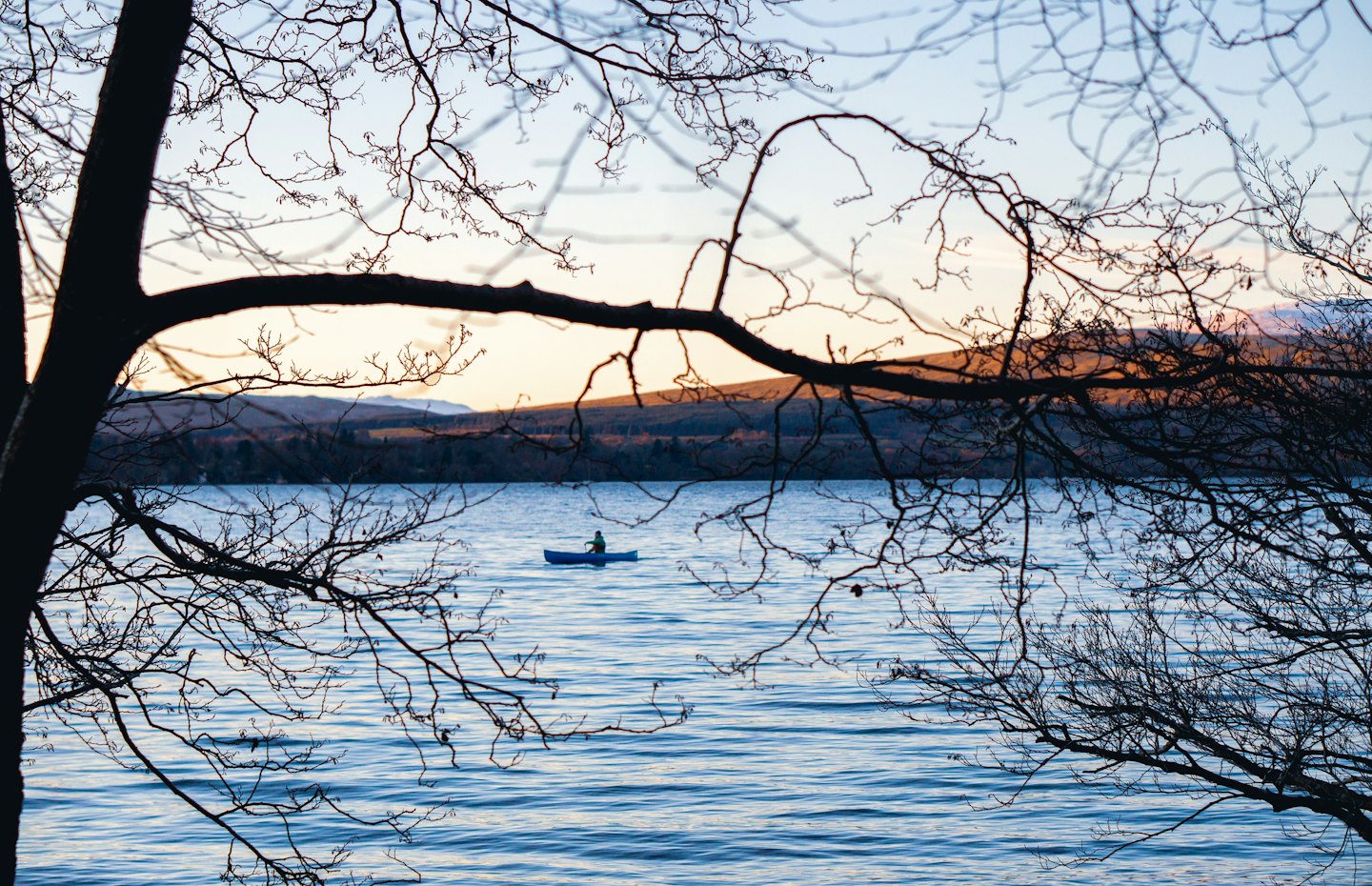 Person paddles a blue canoe across a calm lake.