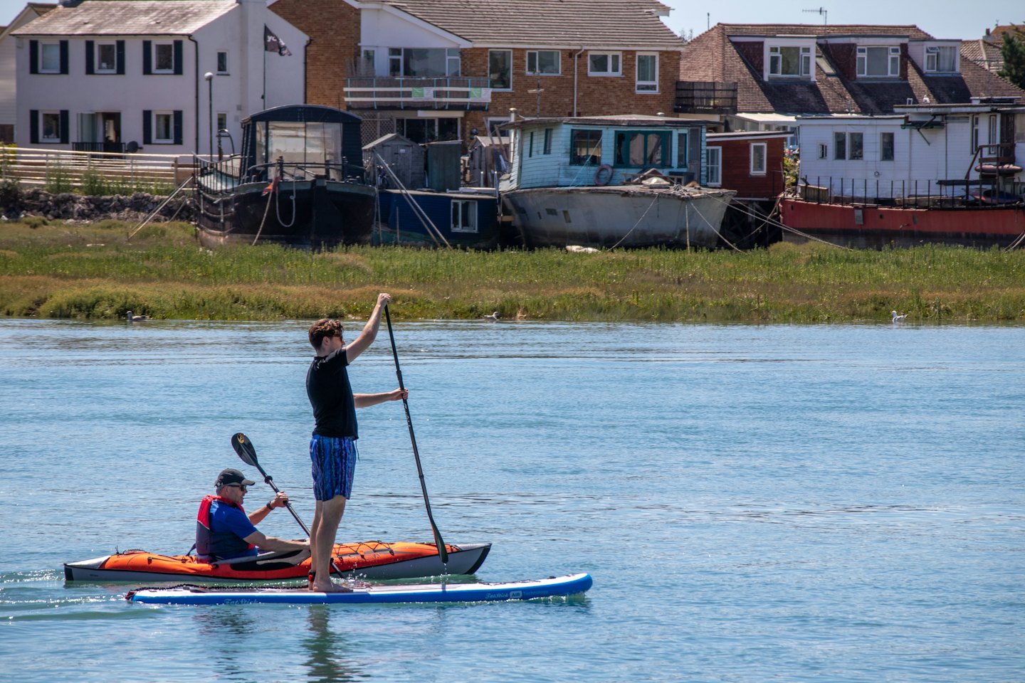 Two men paddle their kayak and paddleboard on a river.