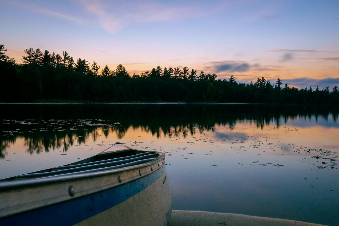 A weathered canoe rests on a calm lake at sunrise.