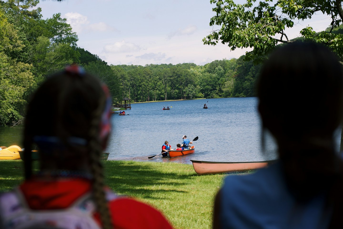 People paddle canoes and kayaks on a calm forest lake.