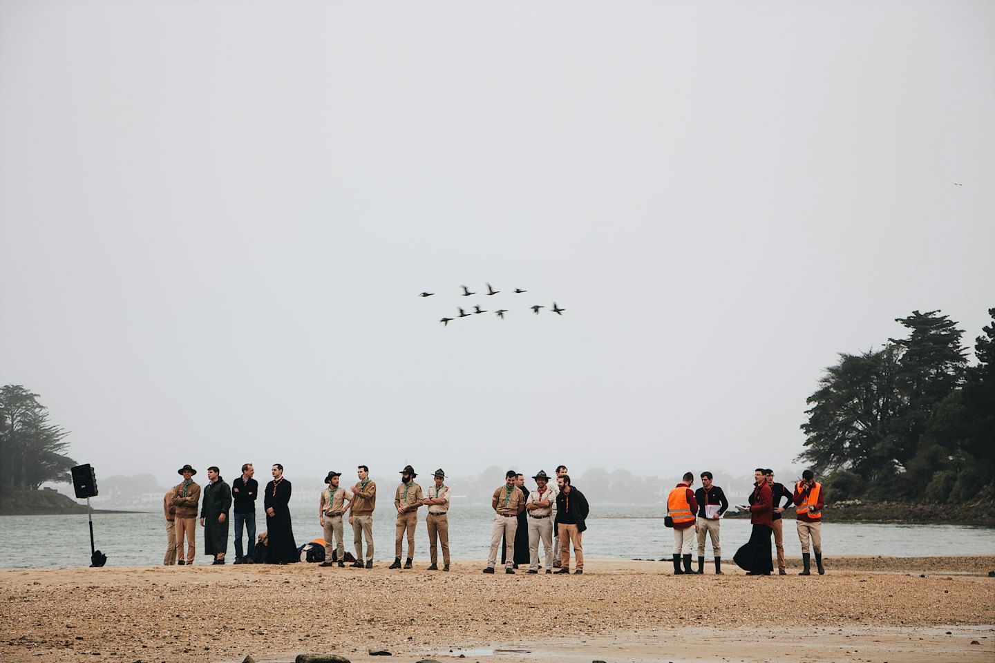 A group of people standing on the sandy coastline talking.