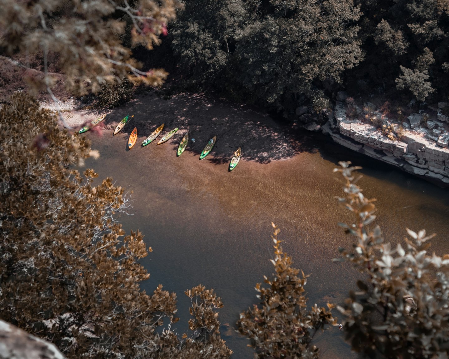 Colorful kayaks and canoes rest on a sandy riverbank.