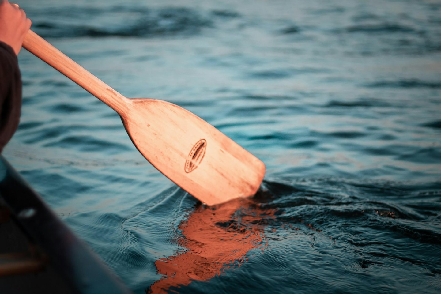 Hand holding wooden paddle entering calm water.